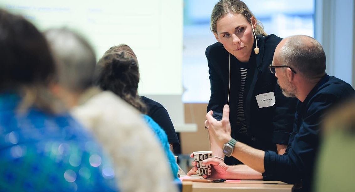 Två personer i ett fokuserat samtal under en presentation.